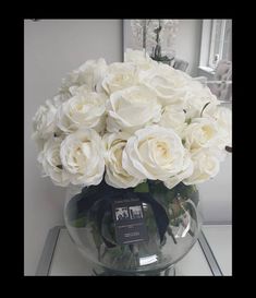 a vase filled with white flowers sitting on top of a glass table next to a mirror