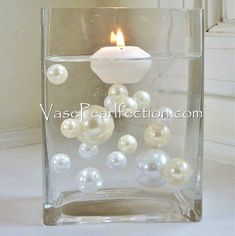 a glass vase filled with pearls and a lit candle