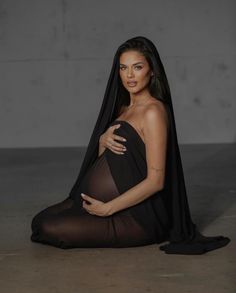 a woman sitting on the ground with her arms around her body and wearing a black dress