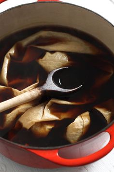 a red pot filled with liquid and wooden spoon on top of a white tablecloth