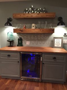 a wine cooler in the middle of a kitchen with shelves above it and glasses on top