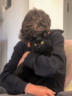 a woman holding a black cat in her arms while sitting on top of a couch