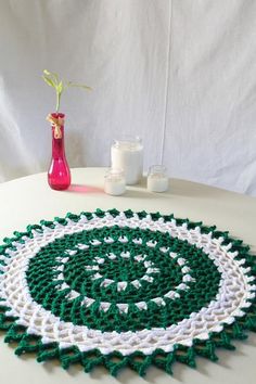 a green and white crocheted doily sitting on top of a table next to a vase