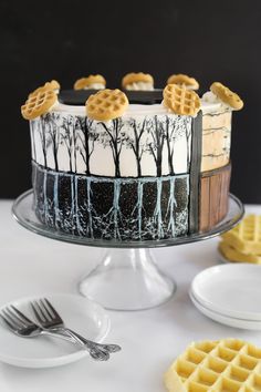 a cake decorated with trees and waffles on a glass platter next to white plates