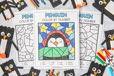 penguin color by number pages with crayons and pencils on the table next to them