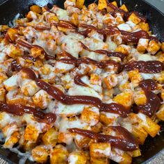 a skillet filled with lots of food covered in cheese and sauce on top of a wooden table