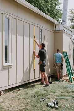 two men are working on the side of a house with siding and tools in front of them