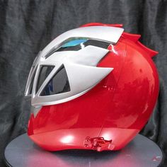 a red helmet with white and green accents on it sitting on a metal stand in front of a black background