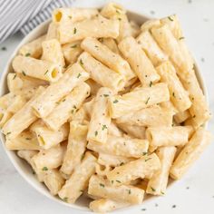 a white bowl filled with pasta and parsley on top of a marble countertop