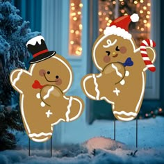 two christmas gingerbreads standing next to each other in front of a house decorated with lights