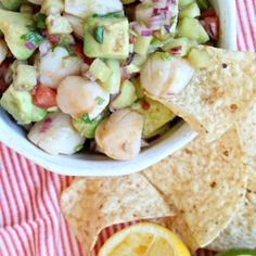 a bowl filled with guacamole and tortilla chips next to sliced lemons