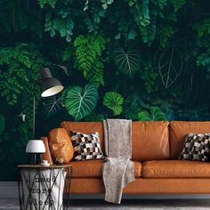 an orange couch sitting in front of a wall with green plants on it and a lamp next to it