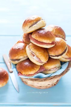 a basket full of ham and cheese sliders with a knife next to it on a blue table