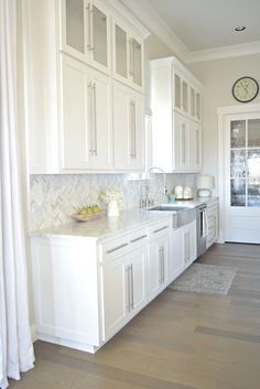 a kitchen with white cabinets and wood flooring next to a clock on the wall