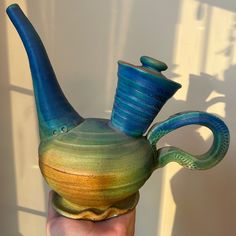 a hand holding a blue and green ceramic teapot