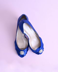 a pair of blue shoes with white flowers on the toe and heel, against a pink background