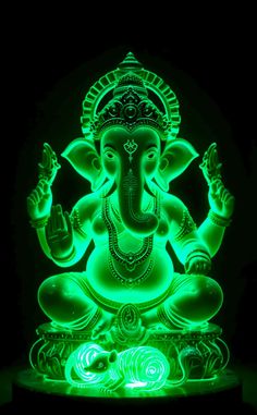 an illuminated statue of the hindu god ganesha in green and blue colors on a black background