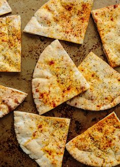 several pieces of flat bread with cheese and seasoning on them sitting on a baking sheet