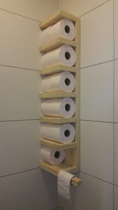 several rolls of toilet paper are stacked on a wooden shelf in the corner of a bathroom