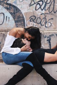 a man and woman are sitting on the wall with their arms around each other as they kiss