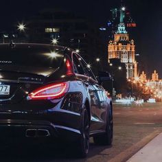 the back end of a car parked in front of a building at night with lights on