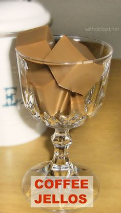 a glass bowl filled with chocolate pieces on top of a wooden table next to a cup