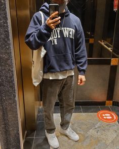 a man standing in front of an elevator looking at his cell phone while wearing a new york yankees hoodie