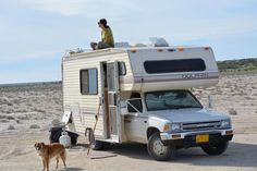 a woman sitting on the roof of an rv with her dog standing next to it