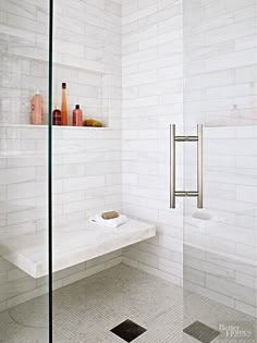 a white tiled bathroom with glass shower doors and shelves on the wall, along with toiletries