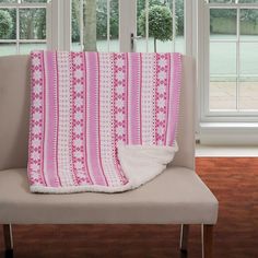 a pink and white blanket sitting on top of a chair next to a window in a living room