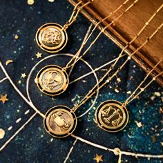 three gold zodiac necklaces sitting on top of a blue cloth with stars in the background