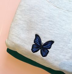 a blue butterfly embroidered on the back of a white t - shirt with green trim