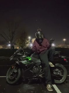 a man sitting on top of a motorcycle in a parking lot at night with street lights behind him