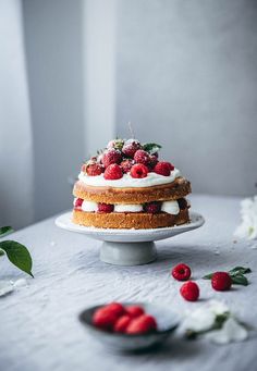 a cake sitting on top of a white table covered in berries and cream frosting