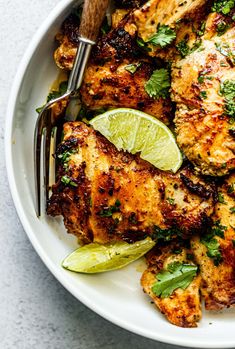 a white bowl filled with chicken and garnished with cilantro, lime wedges