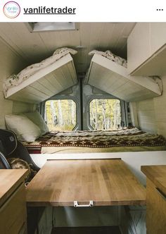 the interior of a camper with two beds and a desk in it, looking out onto the woods