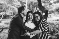 two women and a man hugging each other in black and white photo with trees in the background