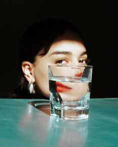 a woman sitting at a table with a glass of water in front of her face