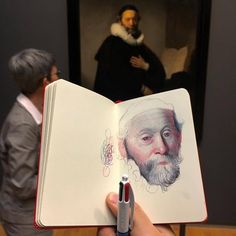 a person holding an open book in front of a man with a painting on it