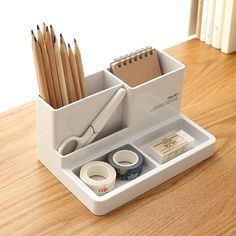 a white desk organizer with pencils, tape and scissors in it on a wooden table