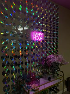 a happy hour neon sign is lit up on the wall behind a table with vases and flowers