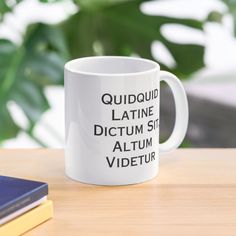 a white coffee mug sitting on top of a wooden table next to a book and plant