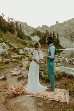 a bride and groom standing on a rug in the mountains