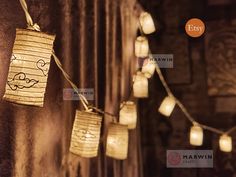 some paper lanterns are hanging on the wall with string lights attached to them and lit up