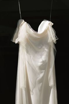 a white dress hanging on a clothesline in front of a black background, with the fabric draped over it