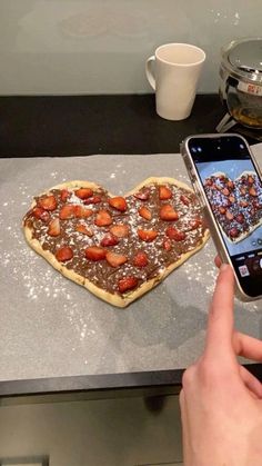 a person taking a photo of a heart shaped pizza on a counter with a cell phone