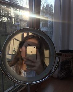 a woman taking a selfie with her cell phone in front of a round mirror