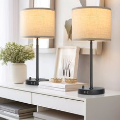 two lamps sitting on top of a white table next to a mirror and vase with flowers