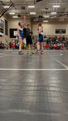 three people on rollerblades in a gym with spectators watching them from the sidelines