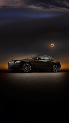 a rolls royce parked in the dark under a cloudy sky at night with an eclipse behind it